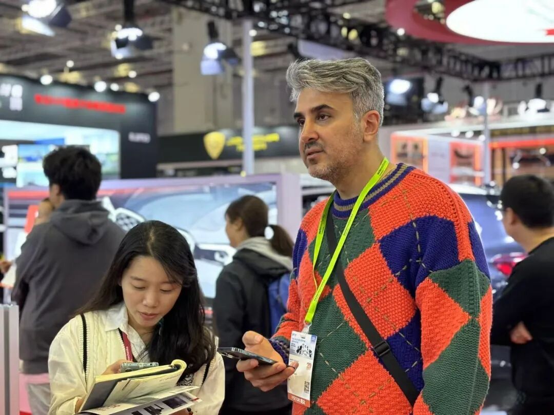 Buyer reading product literature at the WINFOR stand during Automechanika Shanghai 2024, with staff explaining on the spot