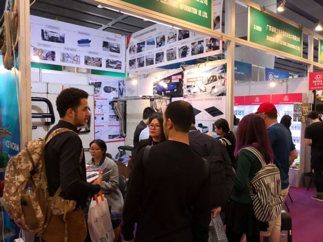 Buyer reviewing pickup bed product literature at the WINFOR Canton Fair booth, with OEM sample orders drawing a crowd