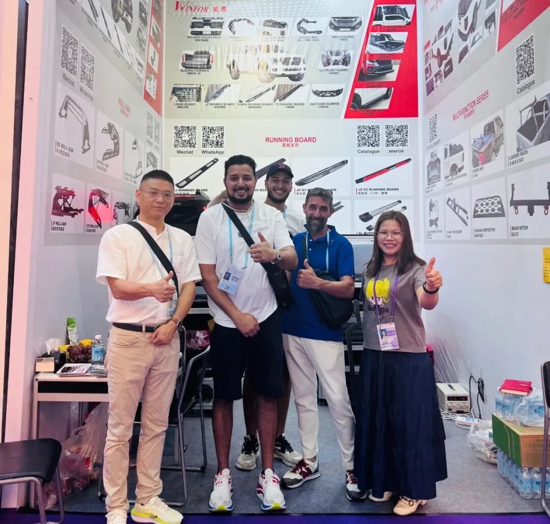 Group photo of the WINFOR booth team and visiting customers inside the Canton Fair stand, with the pickup tonneau cover display wall behind them